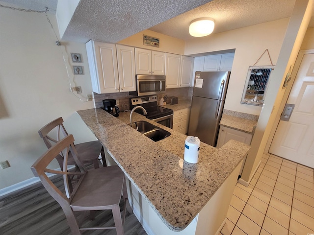 kitchen with appliances with stainless steel finishes, a textured ceiling, white cabinets, and a breakfast bar area