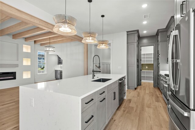 kitchen with light wood-type flooring, a spacious island, stainless steel appliances, sink, and hanging light fixtures