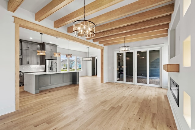 kitchen with light hardwood / wood-style floors, hanging light fixtures, beam ceiling, and an island with sink