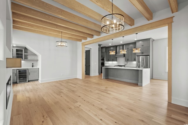 unfurnished living room with light hardwood / wood-style flooring, wine cooler, beamed ceiling, and a chandelier