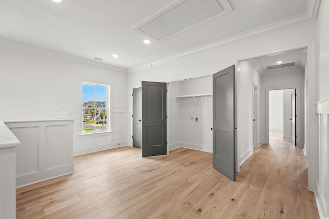 unfurnished bedroom featuring light wood finished floors, visible vents, a decorative wall, attic access, and ornamental molding