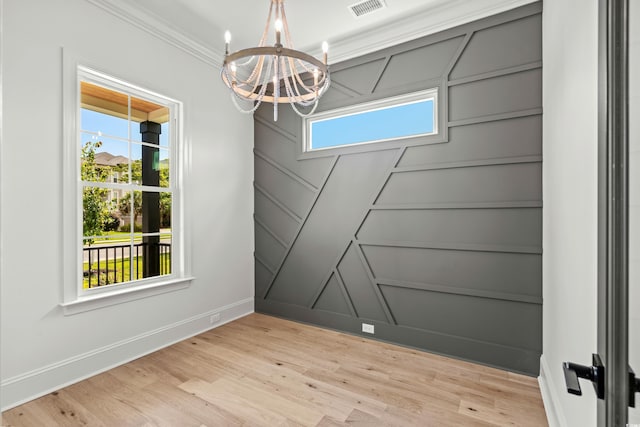 empty room with crown molding, light wood finished floors, visible vents, a decorative wall, and a chandelier