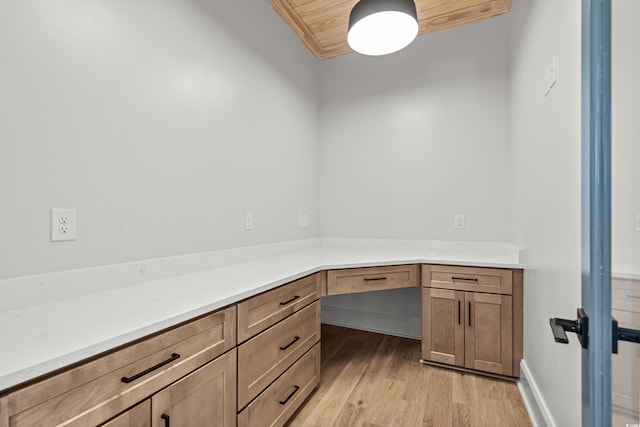 unfurnished office featuring built in desk, light wood-type flooring, and wooden ceiling