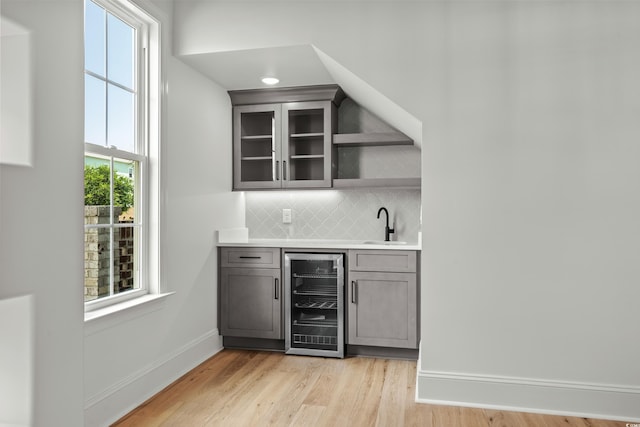 bar with beverage cooler, a sink, baseboards, decorative backsplash, and light wood finished floors