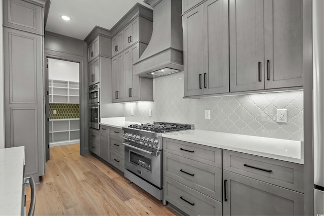 kitchen with custom range hood, high end stainless steel range, gray cabinets, light countertops, and light wood-type flooring