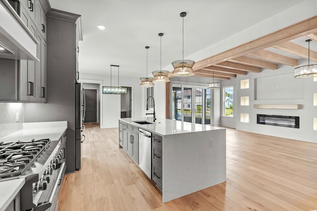 kitchen featuring appliances with stainless steel finishes, beamed ceiling, light hardwood / wood-style flooring, and an island with sink