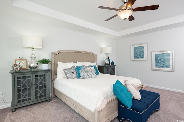 carpeted bedroom with ceiling fan and a raised ceiling