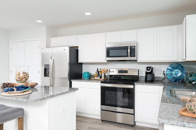 kitchen featuring light hardwood / wood-style flooring, white cabinetry, stainless steel appliances, and light stone counters