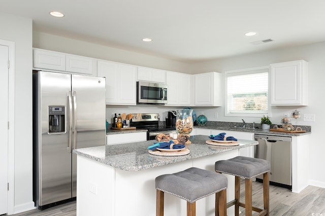 kitchen with light stone countertops, a center island, white cabinetry, appliances with stainless steel finishes, and light hardwood / wood-style floors