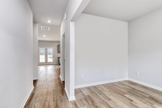 hall featuring baseboards, visible vents, and light wood finished floors