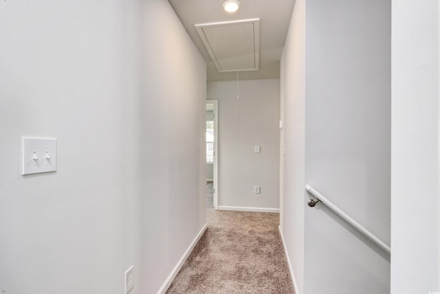 hall with attic access, baseboards, and light carpet