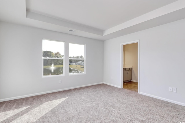 carpeted empty room with a raised ceiling, baseboards, and visible vents