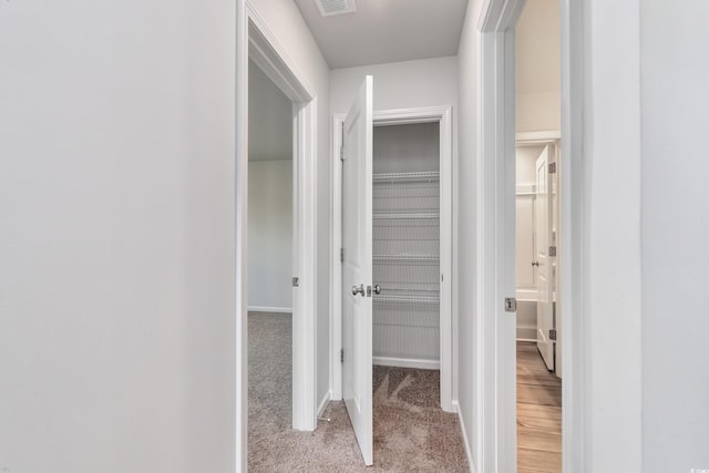 hall featuring light carpet, baseboards, and visible vents