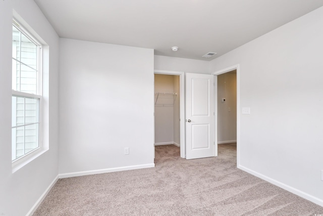 unfurnished bedroom featuring a walk in closet, baseboards, visible vents, and carpet flooring