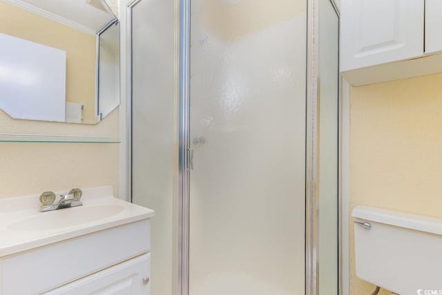 bathroom featuring a shower with shower door, vanity, crown molding, and toilet