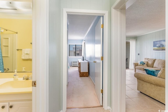 hallway with light carpet, crown molding, sink, and a textured ceiling