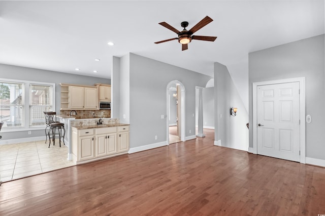 unfurnished living room featuring light wood-style flooring, a sink, ceiling fan, baseboards, and arched walkways