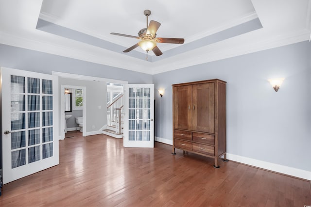 empty room featuring a ceiling fan, stairway, wood finished floors, and a tray ceiling