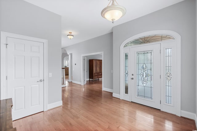 foyer entrance with light wood-type flooring, baseboards, and arched walkways