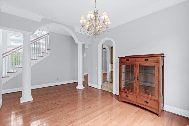 unfurnished living room featuring ornate columns, light hardwood / wood-style flooring, ornamental molding, and an inviting chandelier