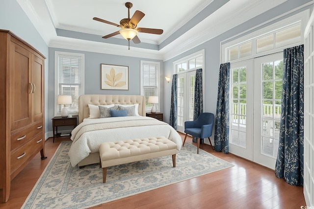 bedroom with crown molding, light wood-style floors, ceiling fan, a tray ceiling, and access to exterior