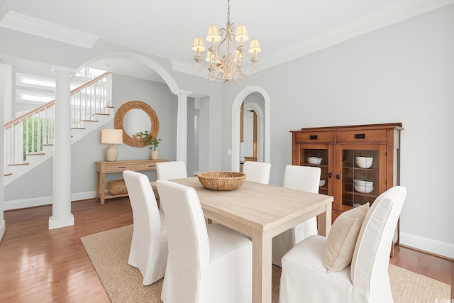 dining area with ornate columns, light wood-style floors, crown molding, and stairway