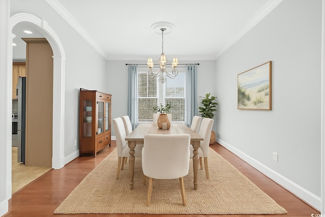 dining room featuring crown molding, arched walkways, a chandelier, and light wood-style floors