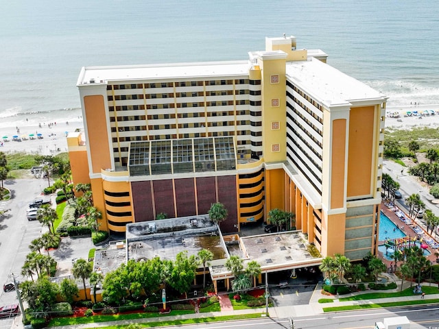 view of building exterior featuring a water view, a swimming pool, and a beach view