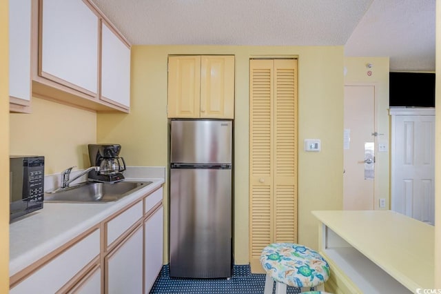 kitchen with light tile patterned flooring, sink, a textured ceiling, and stainless steel fridge