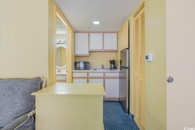 kitchen featuring white cabinets, sink, stainless steel refrigerator, a textured ceiling, and kitchen peninsula