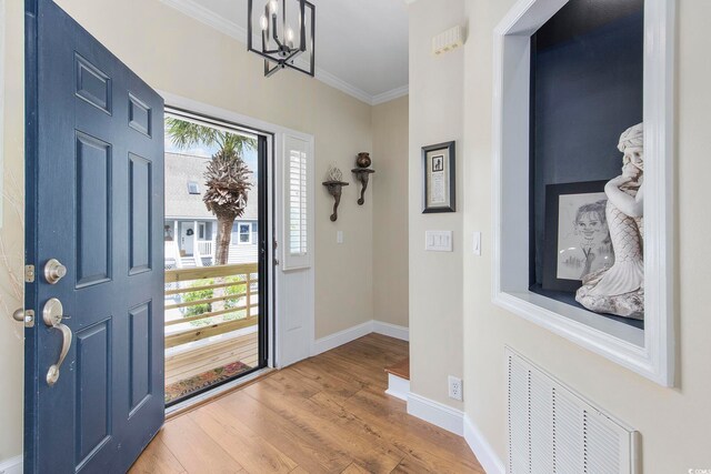 foyer with wood-type flooring, a chandelier, and crown molding