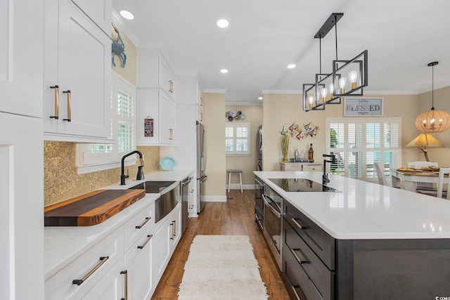 kitchen featuring sink, white cabinetry, decorative light fixtures, an island with sink, and stainless steel appliances