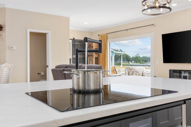 kitchen with light stone counters, crown molding, decorative light fixtures, black electric cooktop, and a barn door