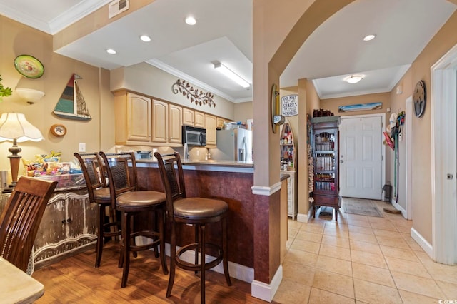 kitchen with a kitchen breakfast bar, stainless steel fridge, light tile patterned flooring, light brown cabinets, and ornamental molding