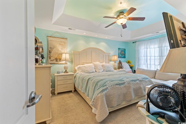 carpeted bedroom with ceiling fan and a raised ceiling