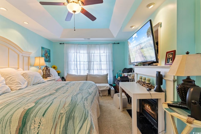 carpeted bedroom with ceiling fan, a raised ceiling, and a fireplace