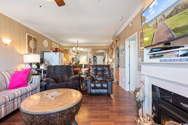 living room featuring ornamental molding, a high end fireplace, ceiling fan with notable chandelier, and dark wood-type flooring