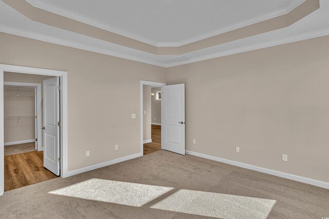 unfurnished bedroom with a walk in closet, a tray ceiling, and light colored carpet