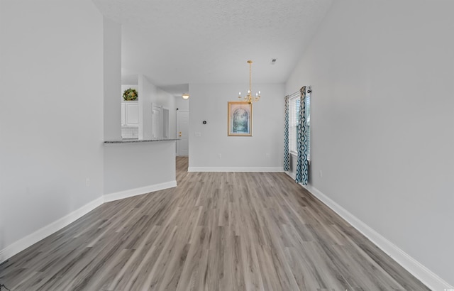 unfurnished living room featuring light hardwood / wood-style flooring, a textured ceiling, and a notable chandelier