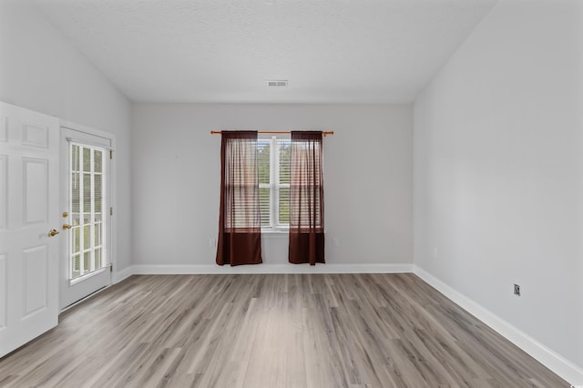 unfurnished room featuring plenty of natural light, a textured ceiling, and light wood-type flooring