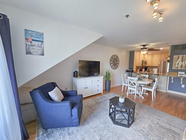 living room with ceiling fan, a textured ceiling, and light hardwood / wood-style flooring