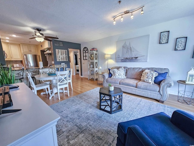 living room with a textured ceiling, ceiling fan, and light hardwood / wood-style flooring