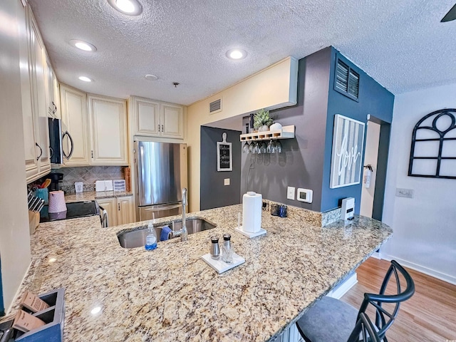 kitchen featuring a kitchen bar, kitchen peninsula, appliances with stainless steel finishes, and a textured ceiling