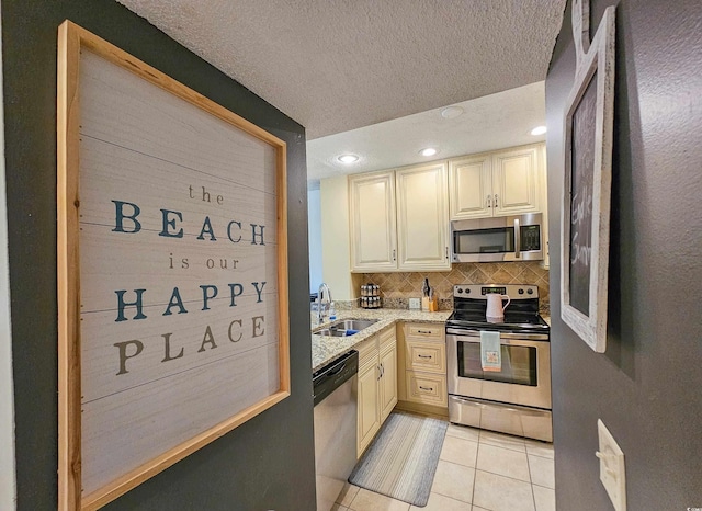 kitchen featuring light tile patterned flooring, sink, cream cabinetry, decorative backsplash, and appliances with stainless steel finishes