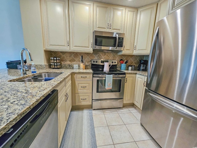 kitchen with appliances with stainless steel finishes, light stone counters, backsplash, light tile patterned floors, and sink