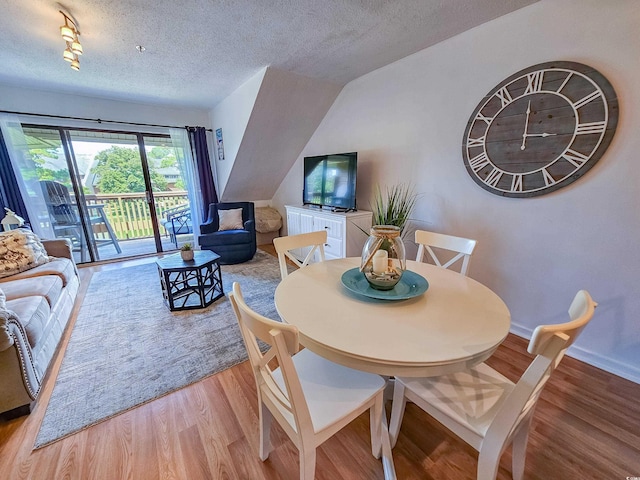 dining area featuring light hardwood / wood-style flooring, vaulted ceiling, and a textured ceiling