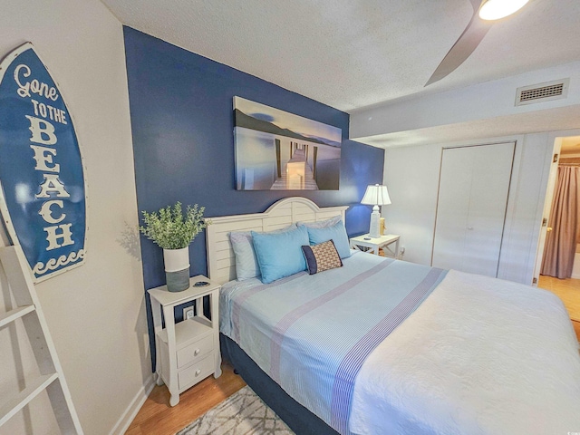 bedroom with a textured ceiling, wood-type flooring, ceiling fan, and a closet