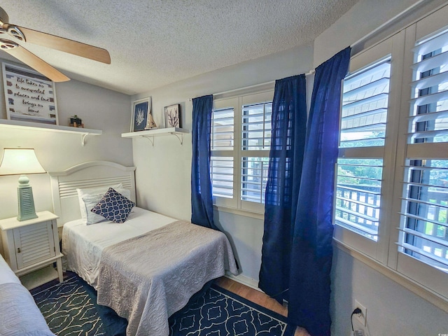 bedroom with multiple windows, wood-type flooring, a textured ceiling, and ceiling fan