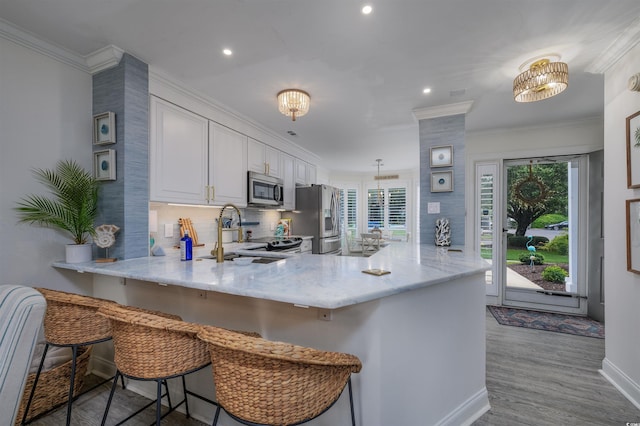 kitchen featuring a kitchen bar, sink, white cabinetry, kitchen peninsula, and stainless steel appliances