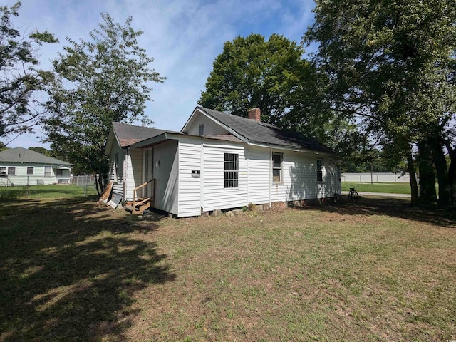 rear view of property with entry steps, a yard, a chimney, and fence